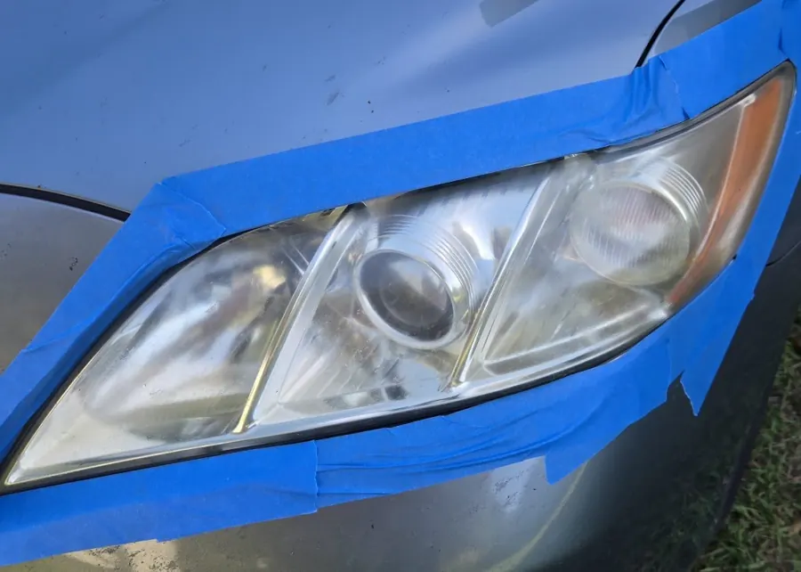 Yellowed, foggy headlight on a Toyota Camry masked with blue tape before restoration