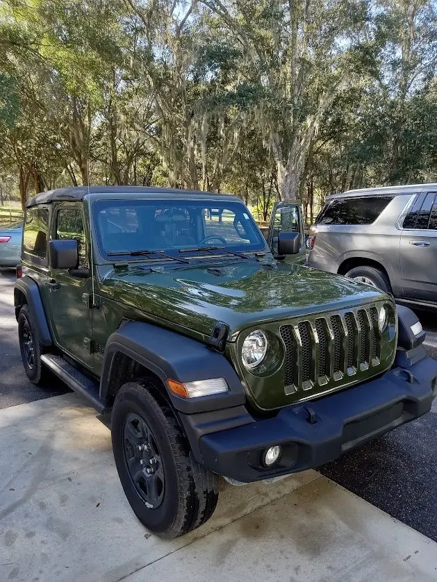 Green Jeep Wrangler parked under oak trees